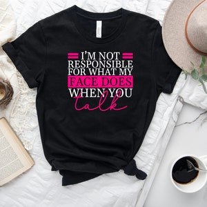 Pode incluir: Camiseta preta com o texto "N&atilde;o sou respons&aacute;vel pelo que meu rosto faz quando voc&ecirc; fala" em letras brancas e rosa.