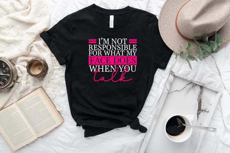 Pode incluir: Camiseta preta com o texto "N&atilde;o sou respons&aacute;vel pelo que meu rosto faz quando voc&ecirc; fala" em letras brancas e rosa.