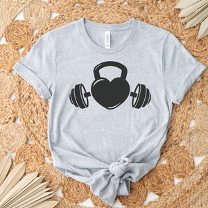 May include: A gray t-shirt with a black graphic of a heart-shaped kettlebell with dumbbells on either side.