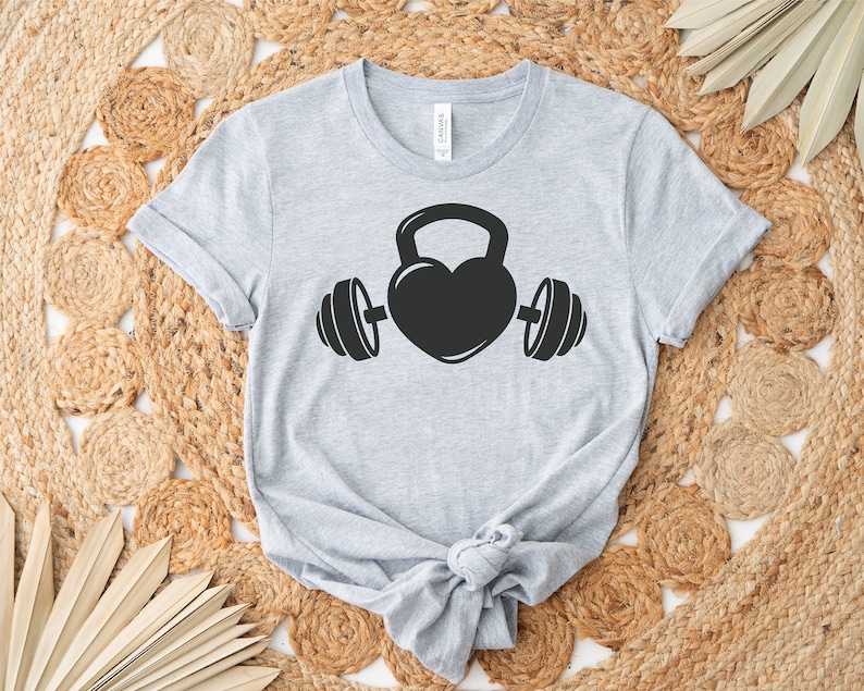 May include: A gray t-shirt with a black graphic of a heart-shaped kettlebell with dumbbells on either side.