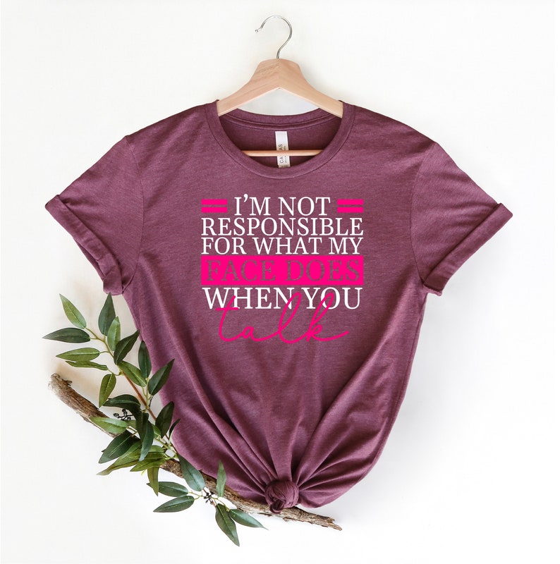 Pode incluir: Camiseta vinho com texto branco que diz "N&atilde;o sou respons&aacute;vel pelo que minha cara faz quando voc&ecirc; fala" com texto rosa que diz "cara faz".