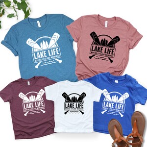 Puede incluir: Varias camisetas de manga corta en varios colores, incluyendo azul, rosa, blanco, burdeos y azul real. Cada camiseta presenta el texto "LAKE LIFE MAKING LIFELONG MEMORIES" con remos cruzados.