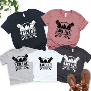 Puede incluir: Varias camisetas en azul marino, malva, gris, blanco y carb&oacute;n. Cada camiseta presenta un gr&aacute;fico en blanco y negro con remos cruzados, &aacute;rboles y el texto "LAKE LIFE MAKING LIFELONG MEMORIES".