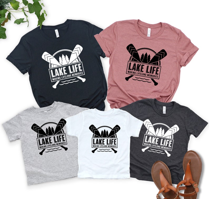 Puede incluir: Varias camisetas en azul marino, malva, gris, blanco y carb&oacute;n. Cada camiseta presenta un gr&aacute;fico en blanco y negro con remos cruzados, &aacute;rboles y el texto "LAKE LIFE MAKING LIFELONG MEMORIES".