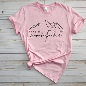 May include: Pink t-shirt with a black graphic of mountains and the text "Take me to the mountains".