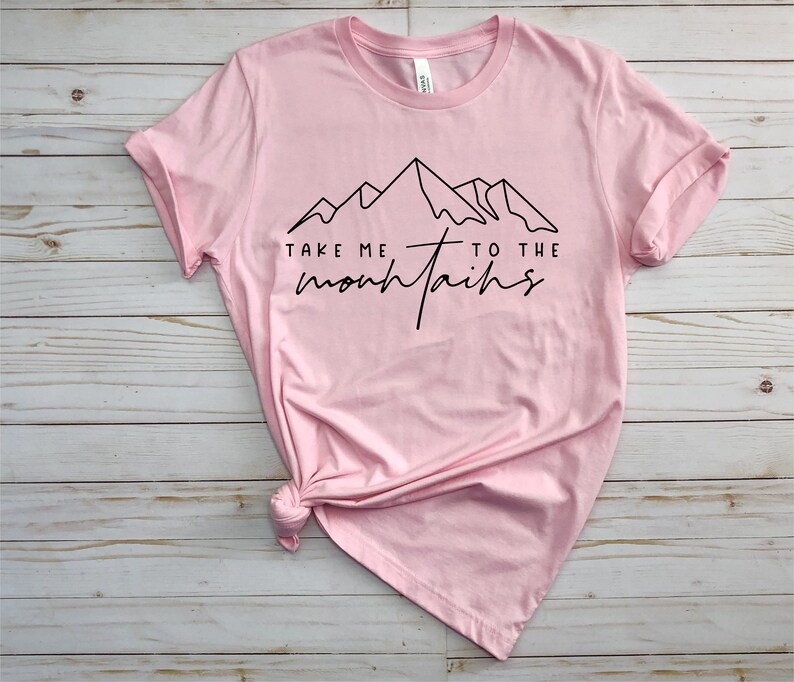 May include: Pink t-shirt with a black graphic of mountains and the text "Take me to the mountains".