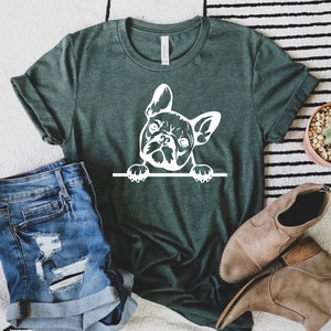 Puede incluir: Una camiseta verde con un gr&aacute;fico blanco de un bulldog franc&eacute;s asom&aacute;ndose por encima de una superficie. El bulldog est&aacute; mirando hacia la derecha.