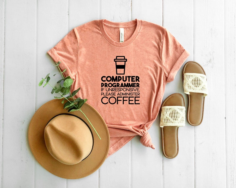 May include: A peach-colored t-shirt with a black graphic of a coffee cup and the text "Computer Programmer. If unresponsive, please administer coffee."