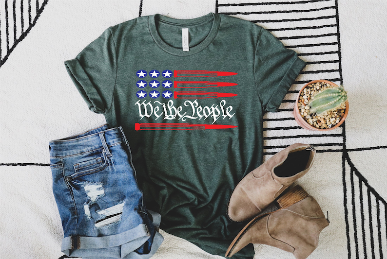 May include: A green t-shirt with a red, white, and blue American flag design. The flag has a red stripe with the words "We the People" in white text.