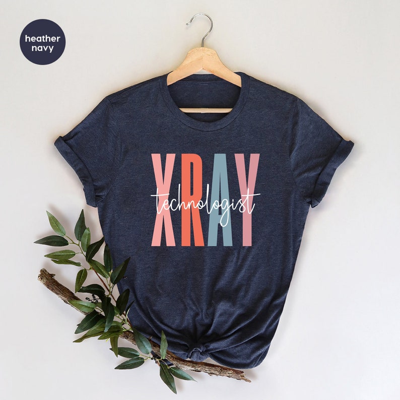 May include: A heather navy blue t-shirt with the text "XRAY technologist" in colorful letters. The letters are stacked vertically and are in shades of pink, orange, blue, and pink.
