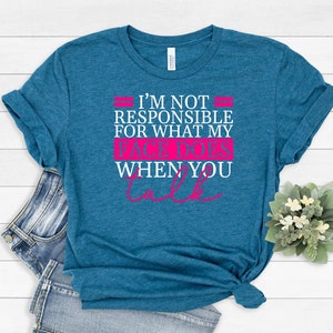 Pode incluir: Uma camiseta azul turquesa com um gr&aacute;fico branco que diz "N&atilde;o sou respons&aacute;vel pelo que meu rosto faz quando voc&ecirc; fala" em rosa.
