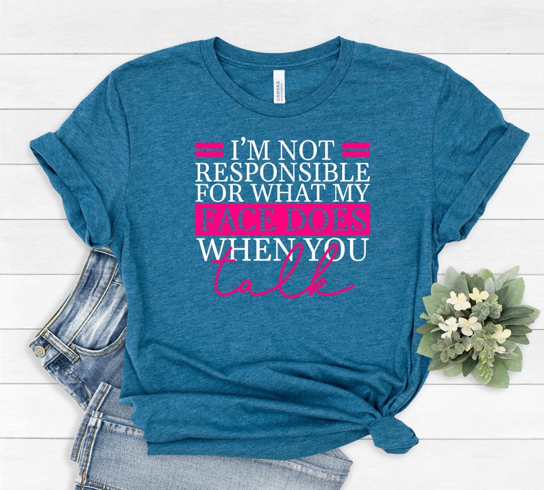 Pode incluir: Uma camiseta azul turquesa com um gr&aacute;fico branco que diz "N&atilde;o sou respons&aacute;vel pelo que meu rosto faz quando voc&ecirc; fala" em rosa.