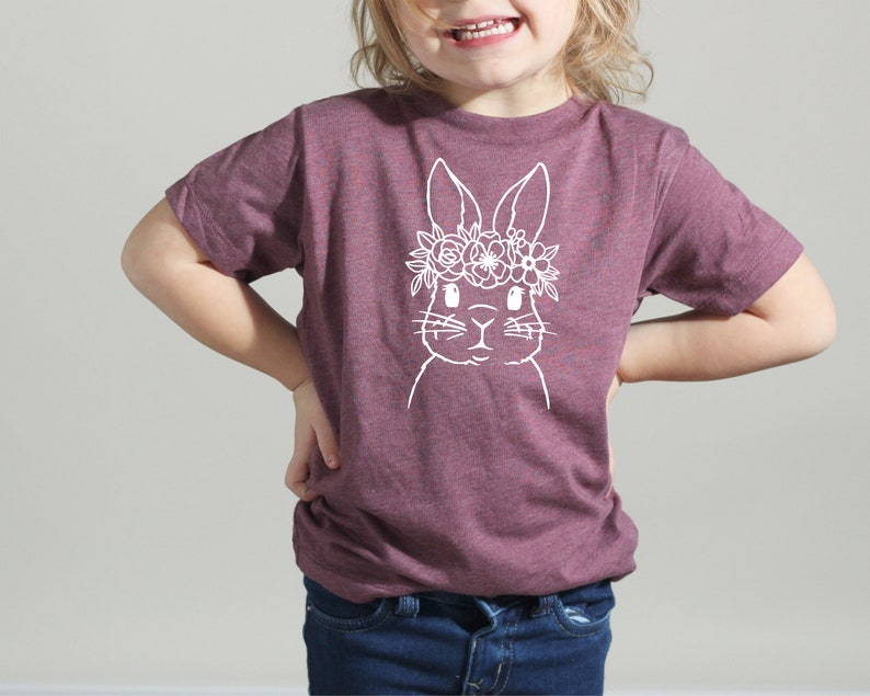 May include: A purple t-shirt with a white outline of a bunny wearing a flower crown.
