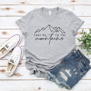 May include: Gray t-shirt with a black outline of mountains and the text "Take me to the mountains".