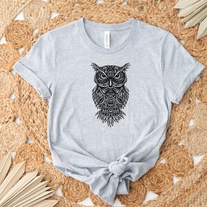 May include: A gray t-shirt with a black and white mandala-style owl graphic. The owl has intricate details and a fierce expression.