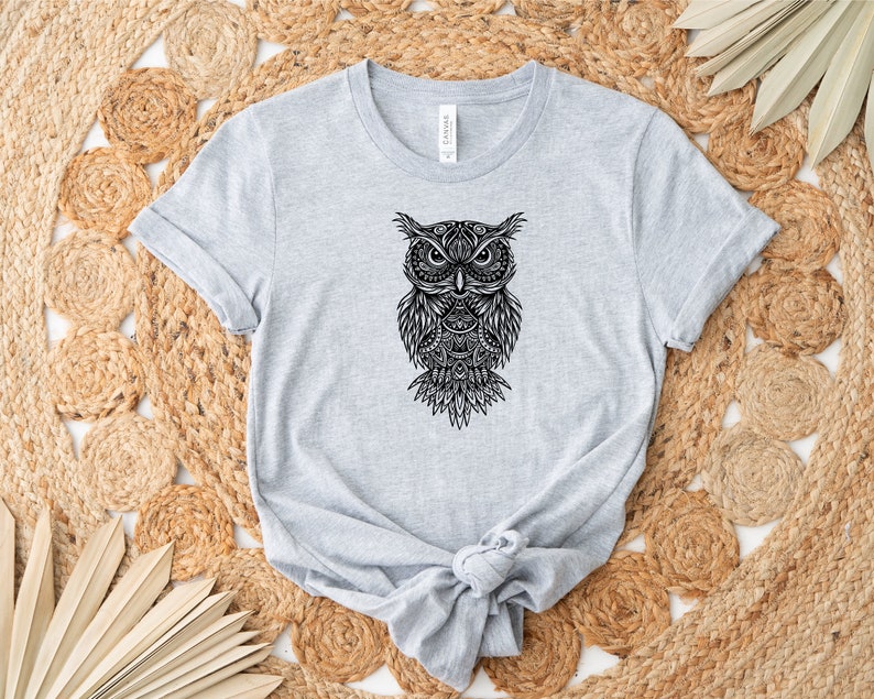 May include: A gray t-shirt with a black and white mandala-style owl graphic. The owl has intricate details and a fierce expression.