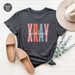 May include: Heather dark grey t-shirt with the text "XRAY technologist" in colorful letters.