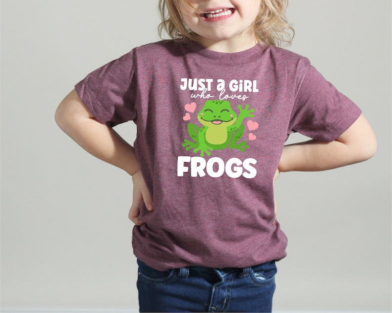 K&ouml;nnte beinhalten: Ein lila T-Shirt mit einem gr&uuml;nen Frosch-Motiv und dem Text "Just a girl who loves frogs".