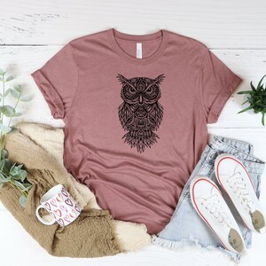 May include: A mauve t-shirt with a black and white mandala-style owl graphic.