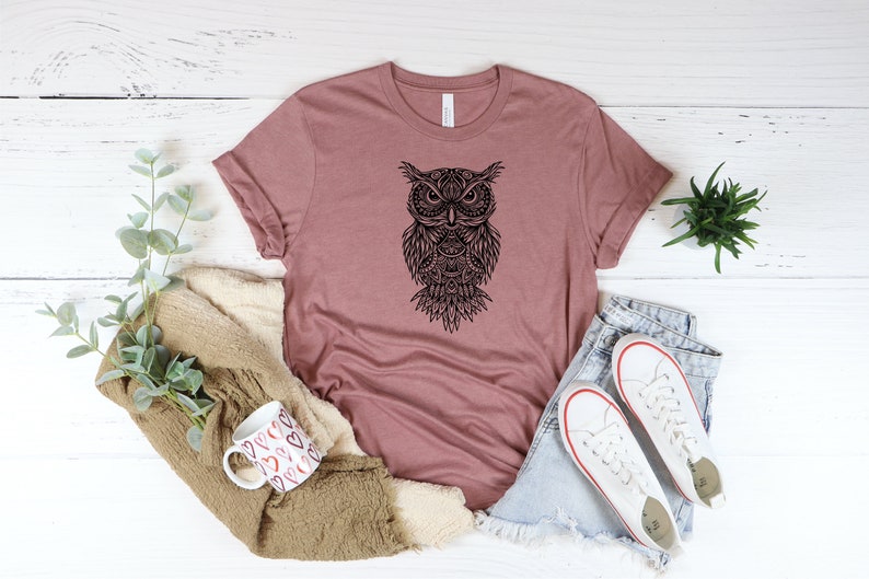 May include: A mauve t-shirt with a black and white mandala-style owl graphic.
