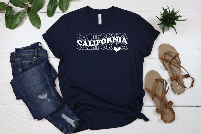 Puede incluir: Una camiseta azul marino con el texto "CALIFORNIA" repetido tres veces en blanco, con un s&iacute;mbolo de coraz&oacute;n al final de la &uacute;ltima palabra.
