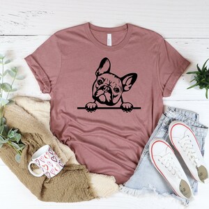 Puede incluir: Una camiseta color malva con una silueta negra de un bulldog franc&eacute;s asom&aacute;ndose por la parte superior de la camiseta.