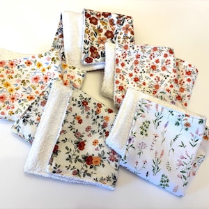 May include: A collection of floral patterned washcloths. Each cloth features a white, fluffy backing and a front with a different floral design. The patterns include various flowers in shades of red, orange, yellow, and purple, set against white backgrounds.