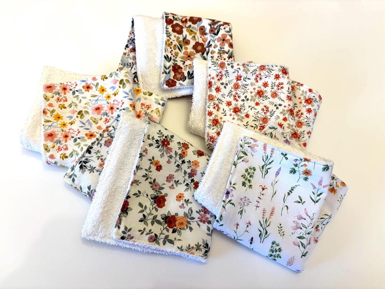 May include: A collection of floral patterned washcloths. Each cloth features a white, fluffy backing and a front with a different floral design. The patterns include various flowers in shades of red, orange, yellow, and purple, set against white backgrounds.