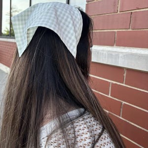 Peut inclure: Une personne avec de longs cheveux noirs portant un haut en crochet blanc et un bandana en vichy vert et blanc noué autour de la tête.