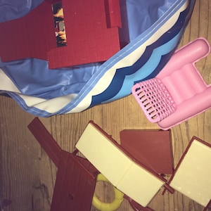 May include: A set of plastic dollhouse furniture, including a red brick fireplace, a pink slide, a brown table, and a yellow life preserver. The furniture is on a blue and white patterned surface.