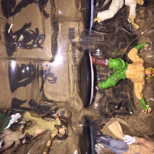 May include: A set of action figures in a clear plastic package. The figures depict various characters in dynamic poses, with detailed costumes and accessories. The figures are in a variety of colors, including white, green, and tan.