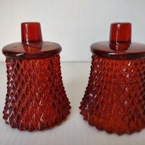 May include: A pair of matching amber-colored glass candle holders featuring a textured diamond pattern across the exterior. Each holder has a wide, circular base that tapers upward toward a smooth, cylindrical top opening for a candle.