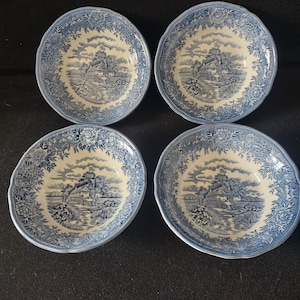 May include: Four blue and white ceramic bowls with a landscape design. Each bowl features a scalloped edge and a detailed floral border. The central image depicts a rural scene with a house, trees, and water.