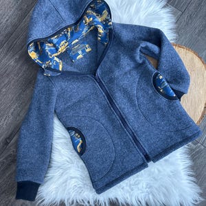 Könnte beinhalten: Eine blaue Kapuzenjacke mit Reißverschluss und einem gemusterten Futter. Die Jacke hat zwei Taschen auf der Vorderseite und einen schwarzen Besatz an der Kapuze und den Ärmelbündchen.
