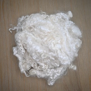 May include: A close-up of a pile of white wool fibers. The wool is soft and fluffy, and it appears to be natural.