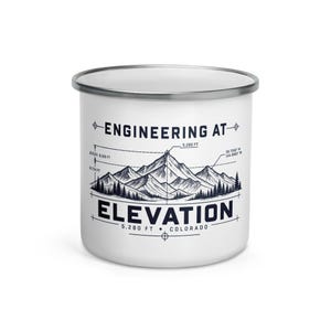 Puede incluir: Una taza de camping de esmalte blanco con borde plateado que presenta un gráfico azul oscuro de picos montañosos, pinos y diagramas técnicos. El texto dice "ENGINEERING AT ELEVATION" con "5,280 FT" y "COLORADO" impresos debajo.