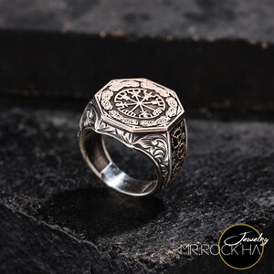 May include: A silver ring with an octagonal face featuring a detailed engraved compass design. The compass is surrounded by a decorative border and the ring band is also engraved with intricate patterns.