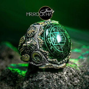 May include: A silver ring with a large green gemstone set in a detailed, ornate design. The gemstone features a star of David and intricate script.
