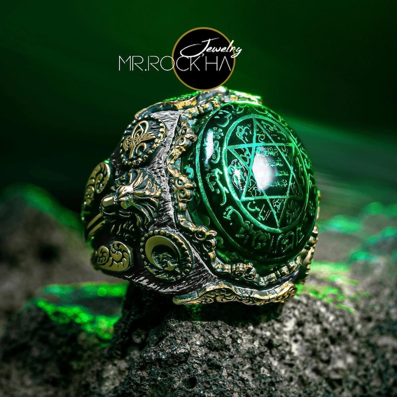 May include: A silver ring with a large green gemstone set in a detailed, ornate design. The gemstone features a Star of David and intricate script.