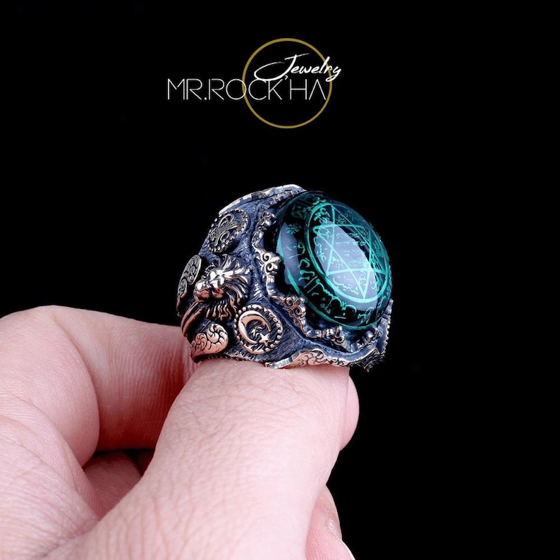 May include: A silver ring with a green stone featuring a pentagram design. The ring has intricate details including a lion head and other decorative elements.