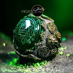 May include: A silver ring featuring a large green gemstone with a star-shaped design and intricate details. The ring also has a wolf head design and other decorative elements.