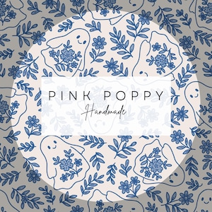 May include: A white circle with a blue and white floral pattern featuring ghosts. The text "PINK POPPY Handmade" is in the center of the circle.