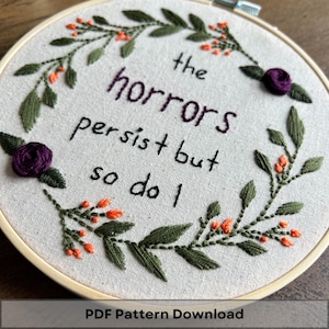 Puede incluir: Arte de bordado en aro con una corona de flores y la cita "los horrores persisten pero yo también".