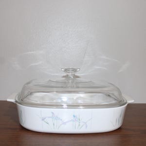 May include: White casserole dish with a clear glass lid. The dish has a floral design in shades of blue and green. The dish is approximately 10 inches long and 7 inches wide.