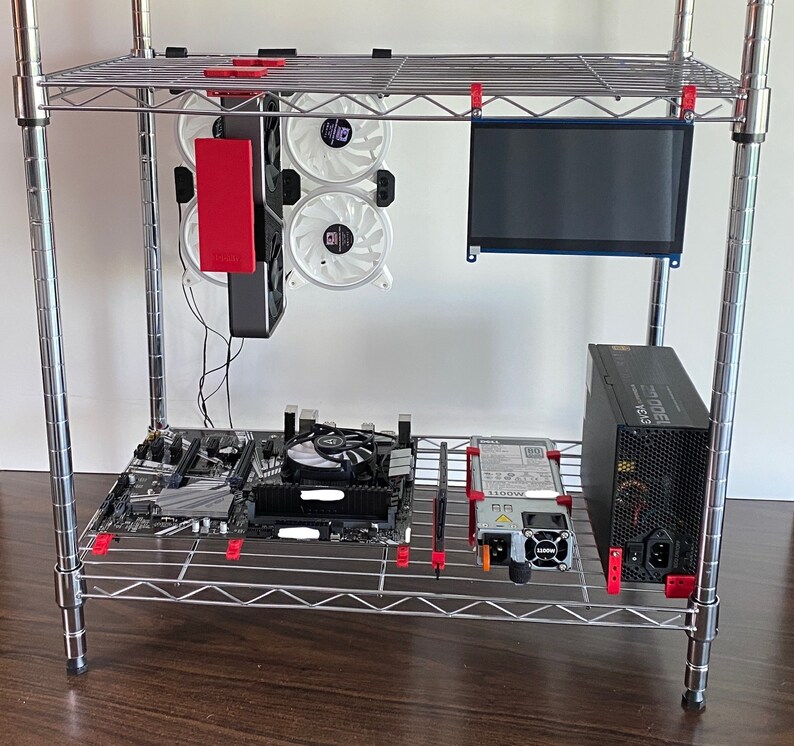 May include: A silver metal shelf unit with a computer motherboard, a power supply, a small monitor, and three white computer fans. The fans are attached to a black metal bracket.