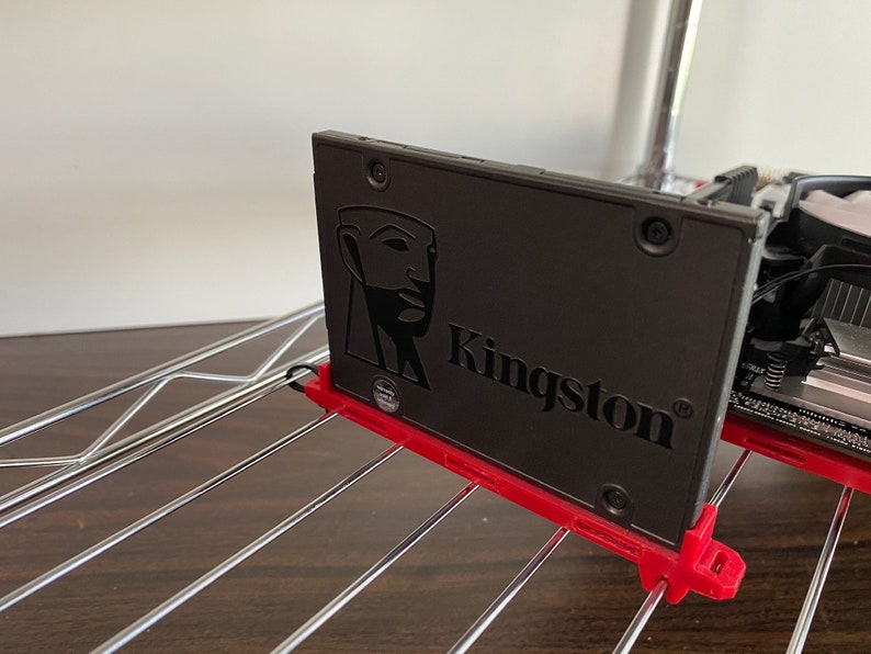 May include: A black Kingston solid state drive (SSD) with a stylised human head logo. The SSD is mounted in a red plastic bracket.