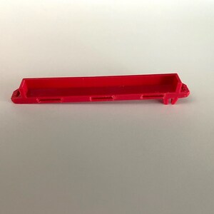 May include: A red plastic toy truck bed with four slots on the bottom.