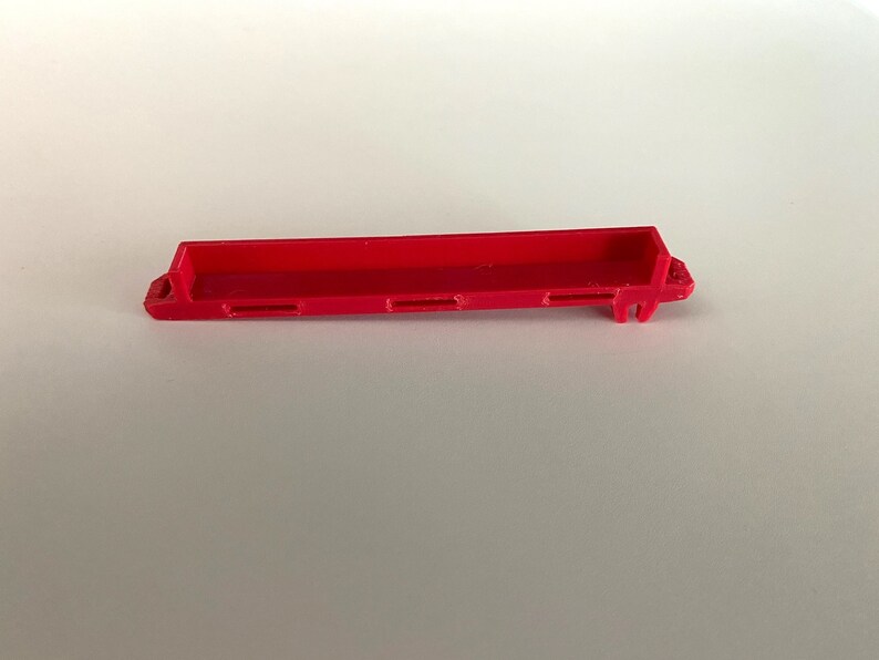 May include: A red plastic toy truck bed with four slots on the bottom.