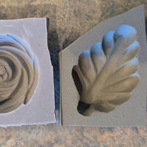 May include: Two gray silicone molds, one shaped like a rose and the other shaped like a leaf.