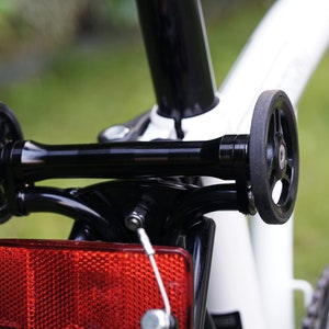 May include: A white bicycle with black wheels and a red reflector. The bicycle has a black metal frame and a black handlebar.